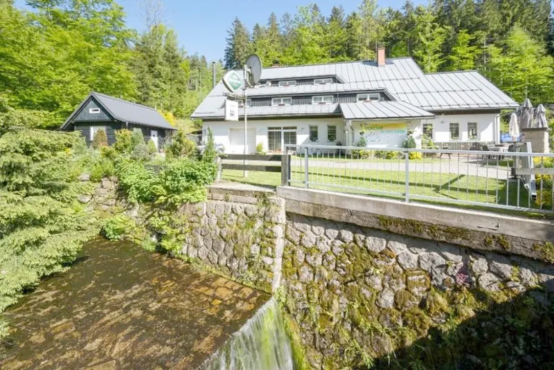 Penzion U Kocoura u potoka v Desné, bílá fasáda a tmavá střecha pod lesem